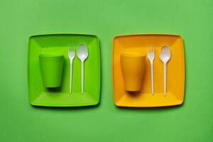 Colorful plastic disposable tableware on green background with copy space. The concept of picnic utensil. Top view. Selective focus. Close-up. photo