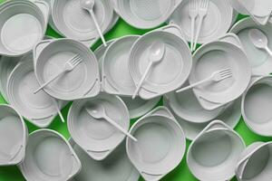 White plastic disposable tableware on green background with copy space. The concept of picnic utensil. Top view. Selective focus. Close-up. photo