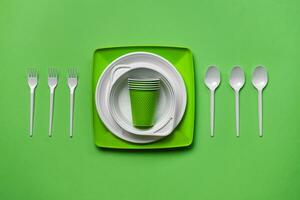 Colorful plastic disposable tableware on green background with copy space. The concept of picnic utensil. Top view. Selective focus. Close-up. photo