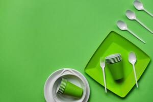 Colorful plastic disposable tableware on green background with copy space. The concept of picnic utensil. Top view. Selective focus. Close-up. photo