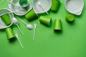 White plastic disposable tableware on green background with copy space. The concept of picnic utensil. Top view. Selective focus. Close-up. photo