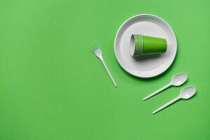 Colorful plastic disposable tableware on green background with copy space. The concept of picnic utensil. Top view. Selective focus. Close-up. photo