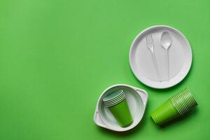 Colorful plastic disposable tableware on green background with copy space. The concept of picnic utensil. Top view. Selective focus. Close-up. photo