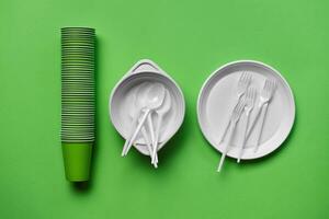 Colorful plastic disposable tableware on green background with copy space. The concept of picnic utensil. Top view. Selective focus. Close-up. photo