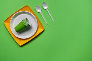 Colorful plastic disposable tableware on green background with copy space. The concept of picnic utensil. Top view. Selective focus. Close-up. photo