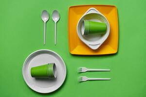 Colorful plastic disposable tableware on green background with copy space. The concept of picnic utensil. Top view. Selective focus. Close-up. photo