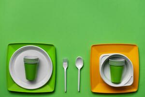 Colorful plastic disposable tableware on green background with copy space. The concept of picnic utensil. Top view. Selective focus. Close-up. photo