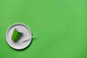 Colorful plastic disposable tableware on green background with copy space. The concept of picnic utensil. Top view. Selective focus. Close-up. photo