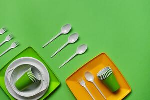 Colorful plastic disposable tableware on green background with copy space. The concept of picnic utensil. Top view. Selective focus. Close-up. photo