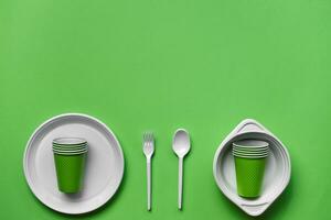 Colorful plastic disposable tableware on green background with copy space. The concept of picnic utensil. Top view. Selective focus. Close-up. photo