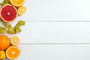 Fresh fruits with tape measure over white wooden background. Top view photo