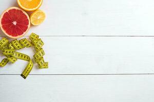 Fresh fruits with tape measure over white wooden background. Top view photo