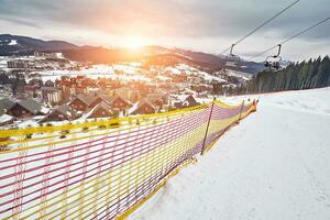 Panorama of ski resort, slope, people on the ski lift, skiers on the piste among green pine trees and snow lances. photo