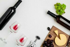 Two wine glasses with red wine,bottle of red wine and cheese on white background.Horizontal view from the top. photo