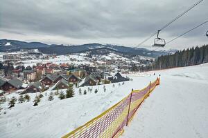 Panorama of ski resort, slope, people on the ski lift, skiers on the piste among green pine trees and snow lances. photo