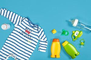 Baby care with bath set. Nipple, toy, clothes, shampoo on blue background top view mockup photo