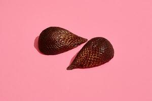 Close up high quality image of bronze salacca halves, fruit composition on pink pastel photo