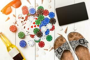 Card deck surrounded by poker chips and scattered seashells on white wooden background with copy space photo