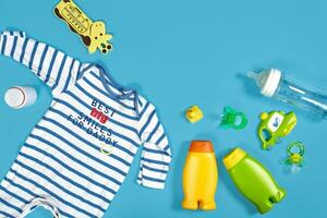 Baby care with bath set. Nipple, toy, clothes, shampoo on blue background top view mockup photo
