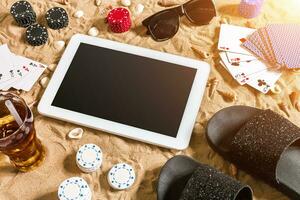 Online poker game on the beach with digital tablet and stacks of chips. Top view photo