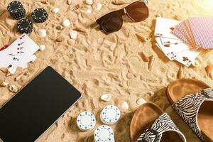 Online poker game on the beach with digital tablet and stacks of chips. Top view photo