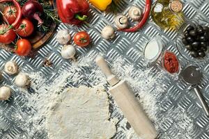 Ingredients and dough for making pizzas with an overhead view on freshly mixed mounds of pastry, a jar of olive oil and pot of tomato sauce, overhead view photo