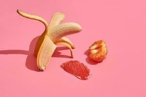 Composition of fresh fruits, whole fresh tasty banana without skin, slice of grapefruit and mandarin on pink background, top view photo