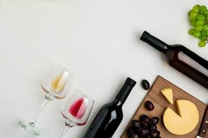 Two wine glasses with red and white wine,bottles of red wine and white wine, cheese on white background. Horizontal view from the top. photo