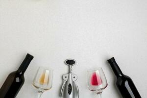 Two wine glasses with red and white wine, bottles of red wine and white wine, corkscrew on white background. Horizontal view from the top. photo