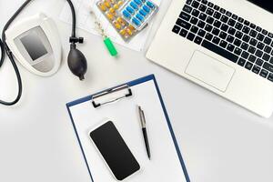 Top view of doctor's desk table, blank paper on clipboard with pen, electronic manometer to measure the blood pressure. photo