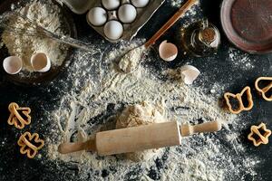 Cooking dough for cookies, butter, eggs, cooking equipment, flour on a black table. Top view with copy space, mockup for menu, recipe or culinary classes. Baking background. photo