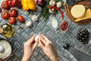 Set of ingredients for pizza and baker's hand smash eggs on metal table photo