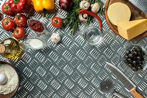 Food ingredients and spices for cooking pizza. Mushrooms, tomatoes, cheese, onion, oil, pepper, salt, egg, grater on metal background. Copy space. Top view photo