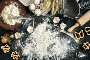 Cooking dough for cookies, butter, eggs, cooking equipment, flour on a black table. Top view with copy space, mockup for menu, recipe or culinary classes. Baking background. photo