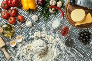 Ingredients and dough for making pizzas with an overhead view on freshly mixed mounds of pastry, a jar of olive oil and pot of tomato sauce, overhead view photo