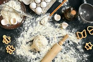 Cooking dough for cookies, butter, eggs, cooking equipment, flour on a black table. Top view with copy space, mockup for menu, recipe or culinary classes. Baking background. photo