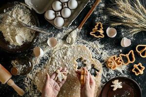 de cerca de un mujer mano con un masa. el mujer es corte un Galleta con un Galleta cortador en el forma de un pequeño humano. ver desde arriba. foto