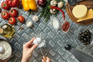 Set of ingredients for pizza and baker's hand smash eggs on metal table photo