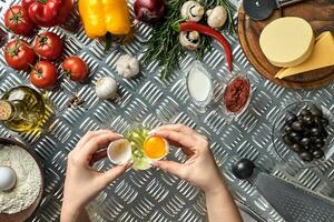 Set of ingredients for pizza and baker's hand smash eggs on metal table photo