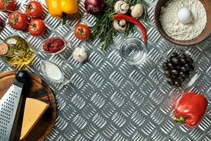 Food ingredients and spices for cooking pizza. Mushrooms, tomatoes, cheese, onion, oil, pepper, salt, egg, grater on metal background. Copy space. Top view photo