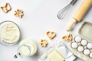 Objects and ingredients for baking, plastic molds for cookies on a white background. Flour, eggs, rolling pin, whisk, milk, butter, cream. Top view, space for text photo