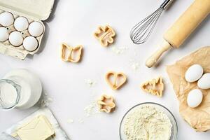 Objects and ingredients for baking, plastic molds for cookies on a white background. Flour, eggs, rolling pin, whisk, milk, butter, cream. Top view, space for text photo