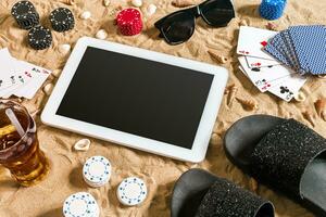 Online poker game on the beach with digital tablet and stacks of chips. Top view photo