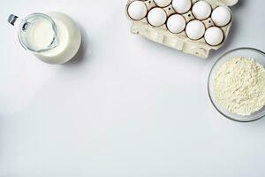 Wheat flour in the glass bowl, cream in a glass jar, chicken eggs - ingredients for the dough, top view photo