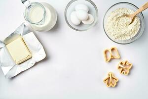 Objects and ingredients for baking, plastic molds for cookies on a white background. Flour, eggs, milk, butter, cream. Top view, space for text photo