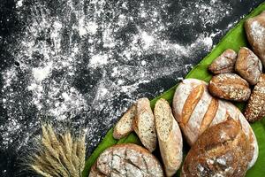 Different bread with flour and spikelets of wheaton black background photo