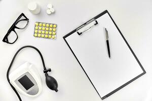 Top view of doctor's desk table, blank paper on clipboard with pen, electronic manometer to measure the blood pressure. photo