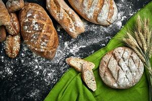 Different bread with flour and spikelets of wheaton black background photo