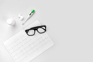 Doctor's desk with thermometer, glasses, pills and cardiogram photo