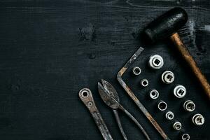 Copy space of working tools on a black wooden surface. Nippers, wrench keys, pliers, screwdriver, hammer. Top view. photo